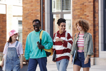 Multiethnic group of young students walking in row together outdoors on college campus and smiling happily
