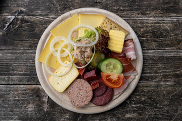 Wooden plate full of cheese, ham, tomato and cucumber on a wooden table