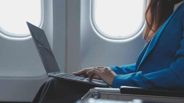 Successful beautiful young asian business woman sits in airplane cabinplane and works on digital tablet with stylus. Flying at first class.