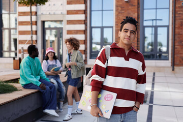 Waist up portrait of Arabian young man as smiling male student standing outdoors in college campus smiling at camera, copy space