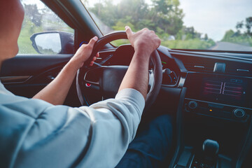 A man is driving with a smile and is happy. On the side of the road there is beautiful nature, the sky is clear.