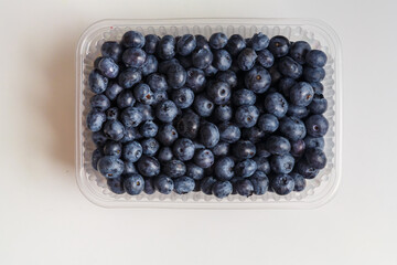 Fresh juicy blueberries in a transparent plastic container with a slide on a white table
