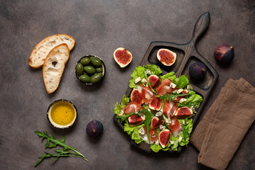 Italian appetizer prosciutto ham , blue cheese, figs, olives and ciabatta on a wooden board, dark rustic background. Top view, flat lay.