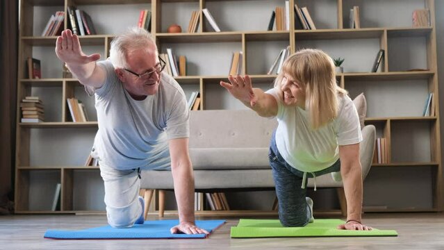  Happy middle-aged couple doing gymnastics and stretching yoga together at home. 