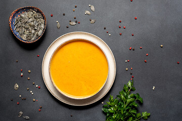 Aromatic hot pumpkin soup with spices, seeds and parsley on black stone table top view. Healthy tasty food concept.