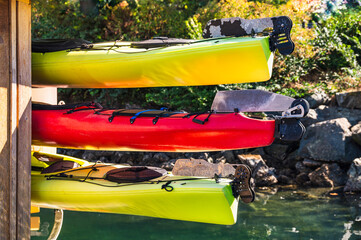 Three colorful plastic canoes are hung on a wooden wall. The rear part with the steering mechanism is visible