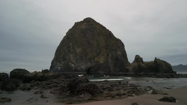 Wide Aerial shot of Haystack Rock beach in coastal town Cannon Beach, Oregon. footage on cloudy day