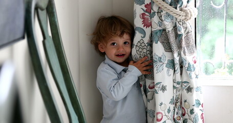 Cute toddler boy hiding behind curtain