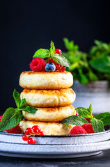 Thick pancakes with cottage cheese, blueberries, raspberries and red currants, decorated with fresh mint delicious breakfast. Black table background