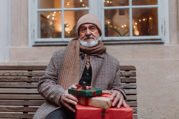 Senior man sitting on a bench, holding a lot of Chrismtas gifts in his hands. Christmas shopping...