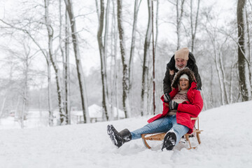 Fototapeta na wymiar Senior couple having fun during cold winter day, sledding down the hill. Winter vacation in the mountains. Wintry landscape.