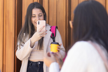 Young woman takes a photo with her smartphone of her friend who is out of focus. Urban youth concept