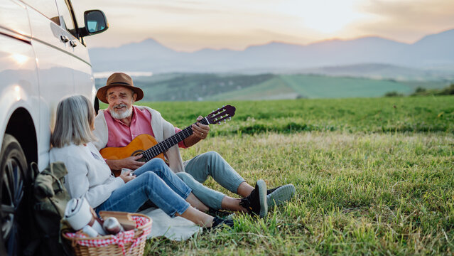 Husband playing the guitar, serenading his wife. Elderly spouses at autumn roadtrip watching the sun set behind High Tatras. Autumn banner with copy space.