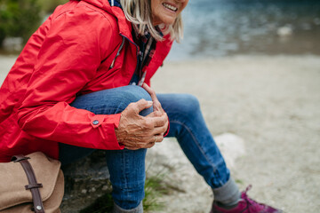 Senior woman injured leg during hike in the mountains. Tourist went off-trail and fell. Eeeling pain under kneecap, also known as Hiker's knee. - obrazy, fototapety, plakaty