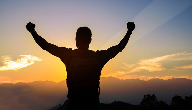 Silhouette of positive man standing on top of the mountain peak with arms raised celebrating his success.Success, victory and winning concept.
