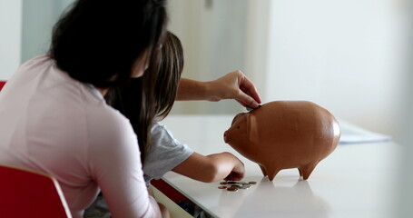 Parent and child saving money by adding coins inside piggy bank