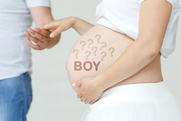 A pregnant woman holds her husband's hand on her stomach with the inscription - BOY, a question mark.
