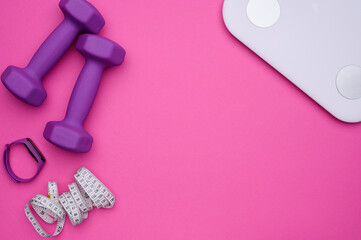 Layout of rubberized dumbbells,measuring tape,fitness bracelet,scales on a pink background,top view. Weight loss concept