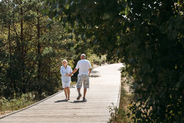 Happy elderly couple walking along a wooden path in the forest