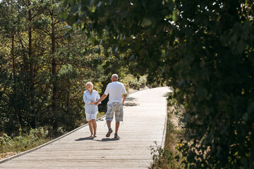 Fototapeta premium Happy elderly couple walking along a wooden path in the forest