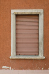 Brown orange stone wall with window and brown closed jalousie shutter, no person, vertical format,