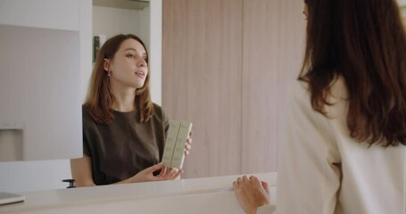 Beautician offer cosmetic product to woman client for face treatment on reception at beauty salon. Cosmetologist recommend professional cream for skin care to young female