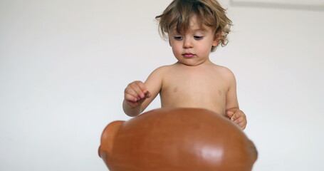 Toddler boy saving money inserting coins inside piggy bank