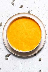 Autumn hot pumpkin soup with cream, parsley and pumpkin seads on white marble table top view. Vertical image.