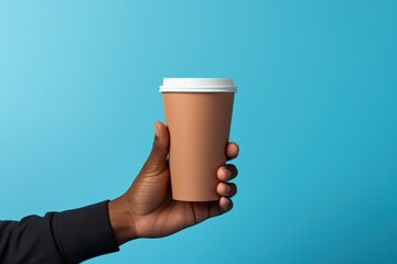 A paper cup of coffee in the dark skin male hand. Isolated. On blue background
