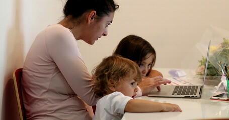 Candid mother multi-tasking at home in front of laptop and parenting kids