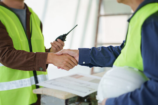 Two engineer businessman handshake after brainstorming blueprint of building in construction site