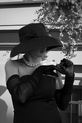 Pregnant beautiful elegant lady in a black dress and a black hat with a large pearl necklace on the...