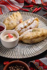 dumplings with cherries in a gray plate on a dark background with jam and sour cream