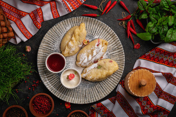 dumplings with cherries in a gray plate on a dark background with jam and sour cream