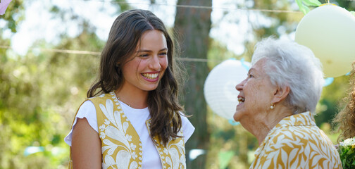 Mature granddaughter and grandmother reunite after a long time, talking. Family gathering at a garden party. Banner with copy space.