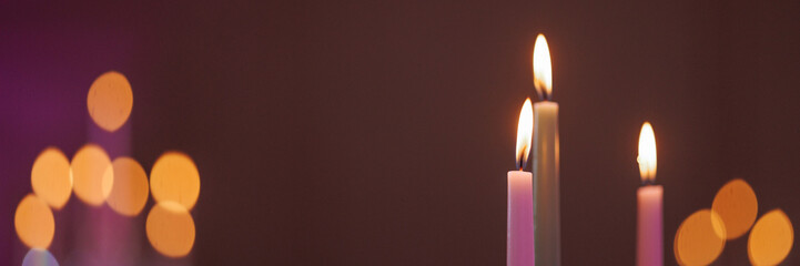 Three long thin candles burning with a copy of the space and a blurred purple background. Banner...
