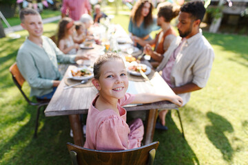 Portrait of girl sitting at the table with family and friends at family garden party. Family...