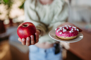 Diabetic woman is choosing between fresh apple and a sweet doughnut. Importance of proper nutrition...