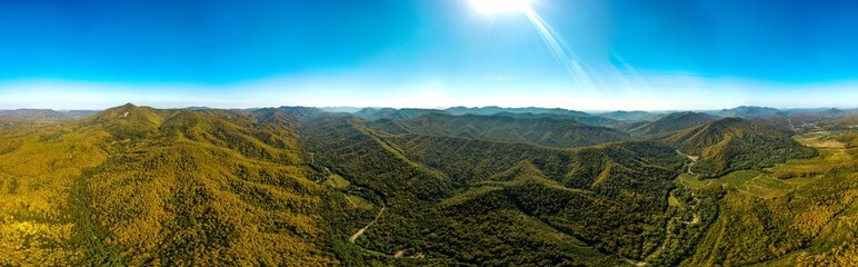 a farm near a river bend surrounded by the Western Caucasus mountains covered with green deciduous forest on a sunny day in early autumn - aerial panorama