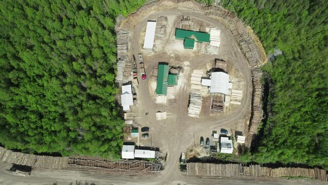 Aerial drone footage of a large timber yard with extensive stacks of processed logs and lumber, roads, storage areas and forestry infrastructure surrounded by forest.