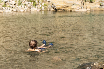 A boy lies in the water of a mountain river. He is resting.