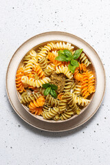 Colorful full grain fusilli pasta with homemade pesto sauce and fresh basil leaves on white stone background top view, vertical image.