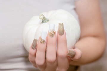 Female hand with long nail design. Glitter gold and white nail polish manicure. Female hand with perfect manicure hold pumpkin
