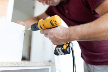 Man worker assembling kitchen wooden elements with cordless screwdriver drill.