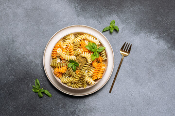 Colorful full grain fusilli pasta with homemade pesto sauce and fresh basil leaves on gray stone...