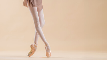 ballerina's feet in pointe shoes stand on a light beige background. copy space.