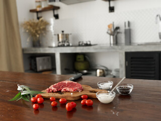 Stylish kitchen, on a wooden table there is a piece of fresh meat with spices, tomatoes and herbs, minimalist interior
