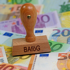 Holzstempel mit dem Aufdruck "BAföG" auf Banknoten