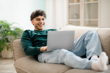 Middle Eastern guy works online at laptop resting at home