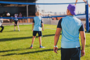 Fototapeta premium Volleyball game, junior teenage school team of kids play volleyball, players on the outdoor playground with net and green lawn grass court, sports children team during the game, summer sunny
